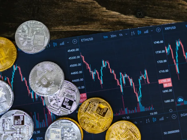 A top view of various cryptocurrency coins on a dark trading chart, showing price fluctuations and market data.
